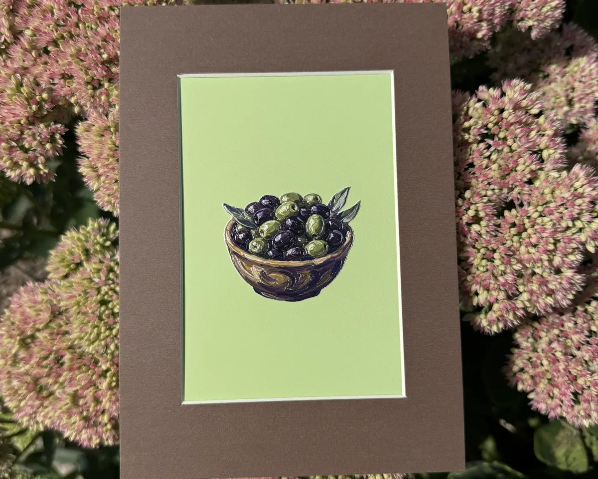 A mini art frame with an olive bowl illustration on a lime green background, resting on pink sedum flowers